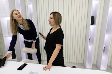 Çağdaş bir ofis ortamında şık bir masada duran iki kadın, canlı bir sohbete dalıyorlar. Yumuşak ışıklandırma, onları çevreleyen modern dekorla dost atmosferi güçlendirir..