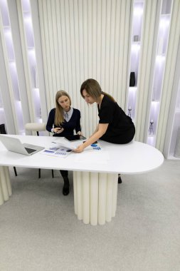 İki kadın modern bir çalışma alanında proje planlaması üzerine bir tartışmaya giriyorlar. Çalışmaları için dizüstü bilgisayar kullanırken şık bir tablodaki belge ve verileri gözden geçirirler..