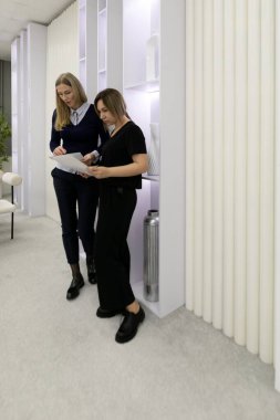 Çağdaş bir ofis alanında iki kadın bir tartışma içindeler. Biri belgeleri incelerken diğeri de not alıyor. Çevre parlak ve iyi ışıklandırılmış, verimliliği teşvik ediyor..