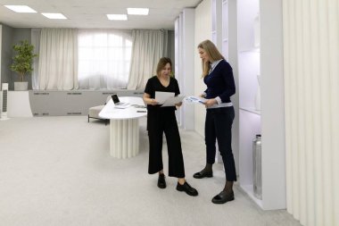 İki meslektaş parlak ve ferah bir ofiste verimli bir tartışmaya giriştiler. Çağdaş bir tasarımla çevriliyken belgeleri gözden geçirir ve fikirleri paylaşırlar..