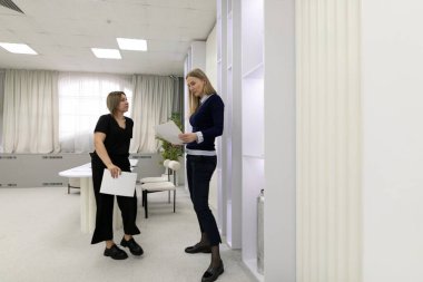 Parlak ve modern bir ofiste, iki kadın belgeleri incelerken tartışmaya girişirler. Biri elinde bir kağıtla ayakta duruyor, diğeri ise dikkatlice işlerinin başında oturuyor..