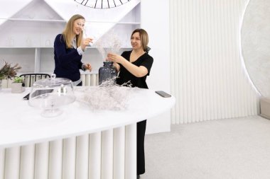 İki kadın şeffaf bir tezgahta çalışıyor, çiçekleri açık bir vazoda düzenliyorlar. Şık ve parlak bir iç mekanda yaratıcı bir sürece giriştiler..