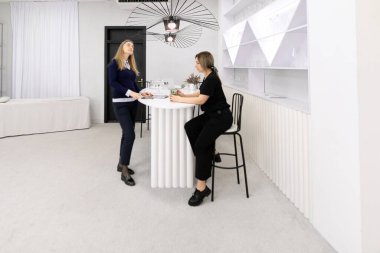 İki kadın şık bir iç tasarım stüdyosunda parlak ve havadar bir atmosferi olan parlak mobilyaları ve çağdaş bir estetiği olan fikirleri tartışıyorlar..