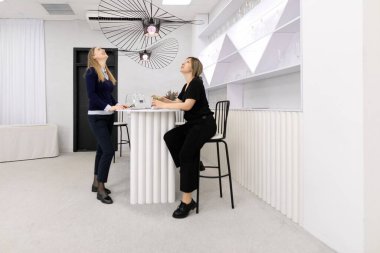 Kadınlar modern bir bar tezgahında ayakta ve oturuyorlar, hareketli bir sohbete dalıyorlar..