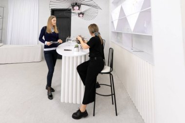 İki kadın, modern bir tasarımı sergilemek için minimalist bir bar tezgahında sohbet ediyorlar. Doğal dekor elementleri davetkar atmosferi arttırır..