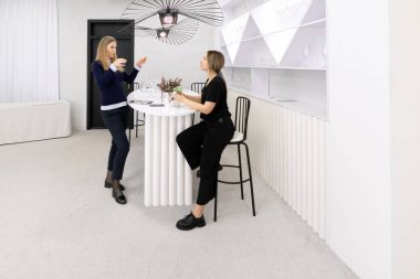 Kadınlar zarif bir dekorla modern bir mekanda hareketli bir şekilde sohbet ederler. Minimalist dekor şık bir bar masası ve sanatsal ışıklandırma içeriyor, davetkar atmosferi artırıyor..