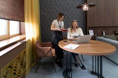 İki kadın şık bir yuvarlak masada ortak bir tartışmaya giriyorlar. Bir kadın dizüstü bilgisayarda defter tutarken, diğeri ise çağdaş dekor ile çevrili..