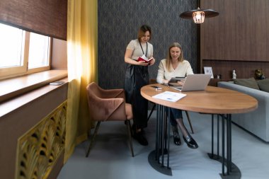 Modern ofis içinde iki kadın üretken bir tartışmaya girişiyor. Biri, her ikisi de dizüstü bilgisayara odaklanmış bir meslektaşının yanında duruyor. Doğal ışık atmosfere sıcaklık katar..