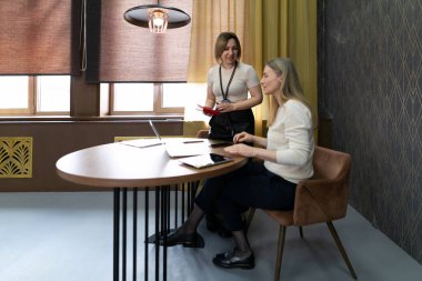 İki profesyonel çağdaş bir ofiste gösterişli bir masada tartışırlar. Bir kişi dizüstü bilgisayarla otururken, diğeri ayakta durup bilgi sunuyor..