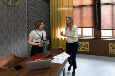 İki kadın modern bir ofis alanında şık bir dekorasyonla canlı bir sohbete girişiyor..