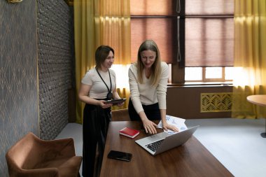 Çağdaş bir ofiste iki kadın ahşap bir masada verimli bir tartışmaya girişiyor. Biri dizüstü bilgisayardaki materyalleri incelerken, diğeri de işbirliğini vurgulayarak tablete notlar alıyor..