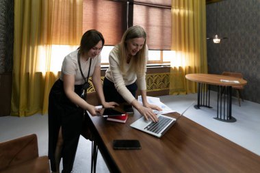 Şık bir ofis alanında, iki kadın bir dizüstü bilgisayarla takım çalışmasına girişiyor, fikir alışverişinde bulunuyor ve parlak güneş ışığı pencerelerden içeri girerken masadaki belgeleri gözden geçiriyorlar..