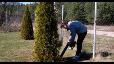 Barışçıl bir açık hava ortamında, bir insan güzel bahar havasının tadını çıkarırken çitleri biçmek ve korumak için çit biçme makinesi kullanır. Bahçe yemyeşil ve bakımlı..