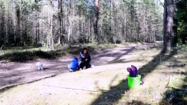 Çocuklar yerde oynarken ve küçük bir köpek yakınlarda dolaşırken bir aile sakin orman patikalarını keşfediyor. Gün aydınlık ve doğa onları çevreleyip neşeli bir atmosfer yaratıyor..