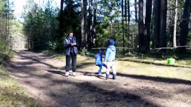 Bir anne, enerjik ve meraklı iki çocukla birlikte orman yolunda yürüyor. Titreşimli çevre ve sıcak güneş ışığı açık hava eğlencesi için neşeli bir ortam yaratır..