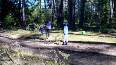 Bir kadın ve iki çocuk uzun ağaçlarla çevrili bir orman yolunda yürüyorlar. Güneşli hava canlı yeşilliği vurguluyor, dışarıda keyifli bir gün yaratıyor..