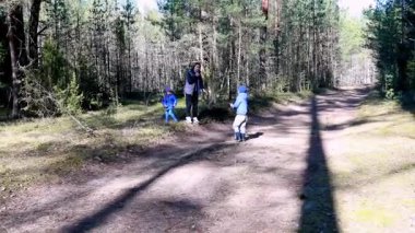 Güneşli bir günde bir yetişkin onlarla meşgul olurken, iki çocuk huzurlu bir ormanda neşeyle oynuyorlar. Bereketli yeşillik, sakin sahnedeki toprak yolu çevreledi..