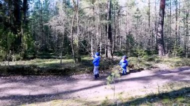 Mavi elbiseli iki çocuk ağaçlarla çevrili bir orman yolunda mutlu mesut dolaşıyorlar. Güneş dalların arasından süzülerek keşif için barışçıl bir atmosfer yaratır..