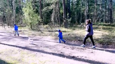 Bir aile güneşli bir günde huzurlu bir orman yolunda gezinir. İki çocuk ebeveynlerinin yanında neşeyle yürürken, küçük bir köpek koşup doğanın tadını çıkarıyor..