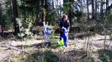 Canlı bir ormanda, iki çocuk bir yetişkinle neşeyle çubuk ve küçük hazineler topluyor. Atmosfer kahkahalarla ve güneşli bir günde doğanın sesleriyle doludur..