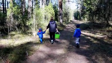 İki çocuk ve bir yetişkin sepet taşıyarak huzurlu bir ormanda yürüyorlar. Doğa gezintisinin, çevreyi gözlemlemenin ve bir köpekle birlikte keşfe çıkmanın tadını çıkarıyorlar..
