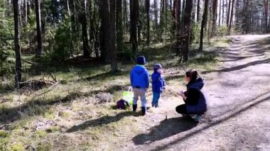 İki çocuk ormanı keşfederken bir yetişkinin rehberliğinde renkli kovalarla eşyalar topluyor. Güneşli bir gün. Açık hava aktiviteleri ve doğa hakkında birlikte bir şeyler öğrenmek için mükemmel..