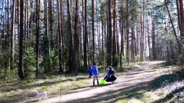Bir aile ormanda güneşli bir günün tadını çıkarırken, iki çocuk oyun oynayıp keşfederken, bir kadın yanlarında küçük bir köpekle diz çöküyor. Doğa huzurlu bir zemin sağlar..