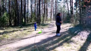 Bir anne ve küçük çocuğu sakin bir orman yolunu keşfediyorlar. Anne yerden küçük eşyalar toplarken çocuk yakınlarda oynuyor. Güneş ışığı ağaçların arasından süzülür.