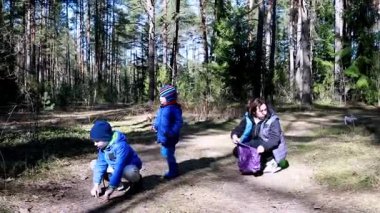 İki çocuk, serin hava için sıcak tutacak şekilde giyinmiş bir orman patikasını keşfedip oynuyorlar. Yakınlarda bir ebeveyn diz çöker, erzakları düzenler ve huzurlu ortamın tadını çıkarır..