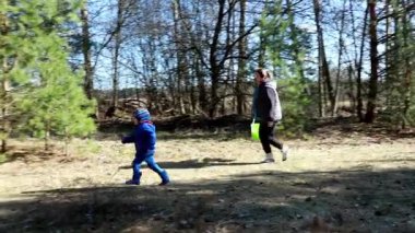 Bir çocuk ve yetişkinin doğa hazinelerini topladığı huzurlu bir ormanda aile gezintisi. Güneş ışığı ağaçların arasından süzülür ve keşif için sakin bir atmosfer yaratır..