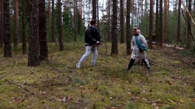 Etrafı uzun ağaçlar ve yemyeşil yemliklerle çevrili sakin bir ormanda mantar arayan bir grup insan orman zemininde farklı noktalara odaklanıyor..