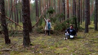 Aile üyeleri, güneşli bir günde ağaçların arasında dalları toplamak ve temiz havanın tadını çıkarmak için ormanda kaliteli zaman geçirirler. Doğayla iç içe olurlar..