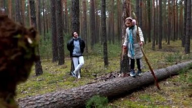 Bir çocuk, bir yetişkin yakınlarda dinlenirken, ormanda düşmüş bir ağaç gövdesi boyunca güvenle yürür. Huzurlu atmosfer uzun ağaçlar ve yeşilliklerle doludur. Keşif için mükemmeldir..