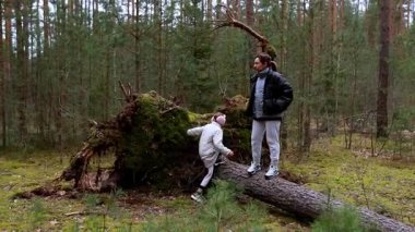İki aile üyesi güzel bir ormanda devrilmiş bir ağaca tırmanarak eğleniyor. Yeşillik onları çevrelemiş, güzel bir sonbahar atmosferi yaratmış..