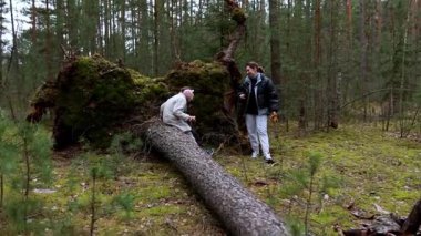 İki arkadaş, büyük bir ağacın yanında, sakin bir ormanda vakit geçirir. Soğuk hava için sıcak kıyafetler giyerken huzurlu ortamın tadını çıkarıyorlar..