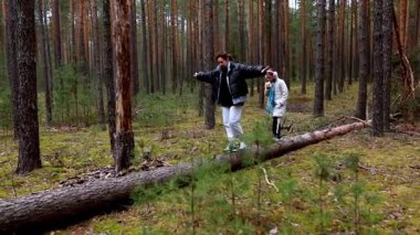 Bir adam ve bir çocuk, dingin bir ormandaki uzun ağaçların arasında devrilmiş bir ağaçta geziniyorlar. Doğadaki eğlenceli anlarının tadını çıkarırken ortam sakin..