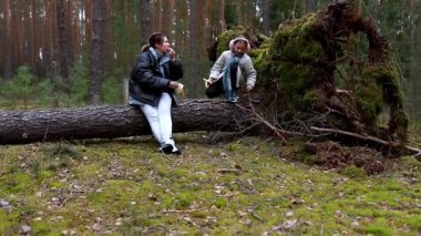 İki birey yemyeşil bir ormanda devrilmiş bir ağaçta oturup atıştırmalıkların tadını çıkarırken, bir çocuk doğanın huzurlu ortamında kendi çevreleriyle neşe içinde etkileşime geçiyor..