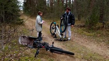 Genç bir kız ve bir adam orman yolunda bisiklet tamirinde birlikte çalışıyorlar. Kız, erkeğin sakin bir sonbahar ayarı için tekerleği ayarlamasını izler..