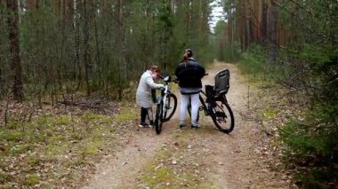 Bir kadın ve bir çocuk sakin bir ormanda bisiklet sürmeye ara veriyor. Uzun ağaçlarla çevrili dar bir patika boyunca durup doğanın huzurlu atmosferinin tadını çıkarırlar..