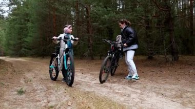 Bir anne ve çocuğu uzun ağaçlarla çevrili bir orman yolunda bisiklet sürerken mola verirler. Sohbet ederken sıcacık giyiniyorlar ve huzurlu atmosferin tadını çıkarıyorlar..