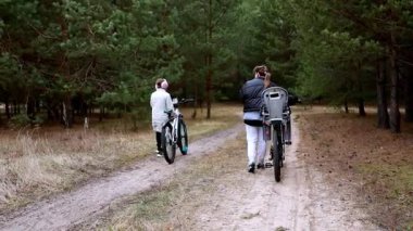 İki birey ağaçlarla çevrili huzurlu bir orman yolunda bisiklet sürmenin keyfini çıkarıyorlar. Atmosfer sakin, mükemmel bir açık hava macerası olacak..