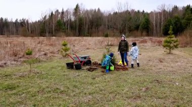 İki çocuk fidanları fidanlarla çevrili bir çayırda fidan dikmekle meşgul. Hava serin, bu da baharın başlarını gösteriyor..