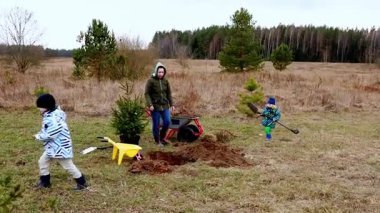 Çocuklar bir ormanla çevrili çimenlik bir alanda genç ağaçlar dikerler. Alet ve el arabası kullanırlar, serin havada doğayla iç içe olurlar..