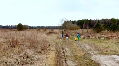 İki birey ağaçlarla çevrili uçsuz bucaksız bir çimenlik alanda çalışıyor. Bulutlu gökyüzü tomurcuklanan doğayla ilkbaharın başlarında olduğunu gösteriyor..
