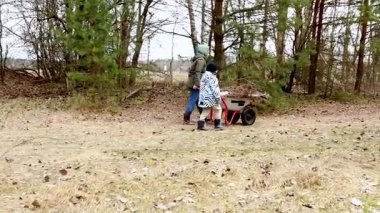 İki çocuk ormanlık alandaki bir bahçeyi temizlemek için birlikte çalışıyorlar. Enkaz toplamak için el arabası kullanıyorlar ve baharda verimli bir günün tadını çıkarıyorlar..