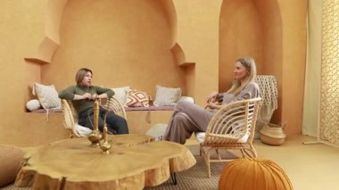 İki kadın şık, sıcak bir iç mekanda oturup, rahat döşemelerle çevrili, anlayışlı bir sohbeti paylaşıyorlar. Uzay konfor ve bağlantı yayar..