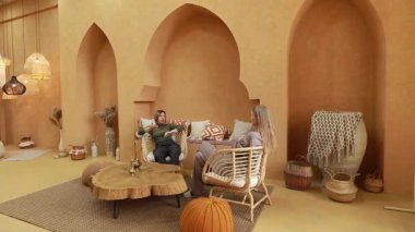 İki birey, benzersiz dekor elementleriyle dolu şık, sıcak tonlu bir mekanda dostça bir tartışmaya girişirler. Ayarda rahat mobilyalar ve rahat bir atmosfer yer alıyor..