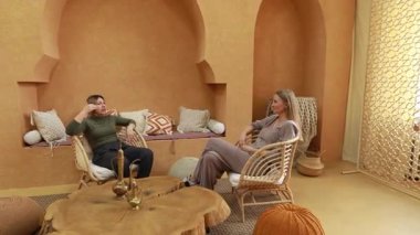 Güzel dekore edilmiş, toprak tonlu bir odada iki kadın düşünceli bir sohbete girişir. Mekan karmaşık detaylar ve rahat koltuklar içeriyor, rahatlatıcı bir atmosfer yaratıyor..