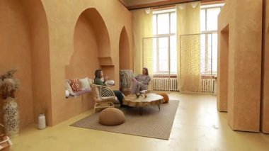 İki insan doğal ışıkla dolu rahat, davetkar bir odada rahat bir sohbete girişir. Uzay yumuşak dokular ve rahatlatıcı bir atmosfer yaratan topraksı tonlara sahiptir..