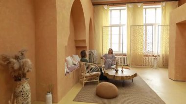 İki arkadaş, doğal elementlerle süslenmiş sıcak, davetkar bir refah ortamında bir anı paylaşıyor. Rahatlatıcı sohbetler samimi odayı doldurur, huzurlu bir ortam yaratır..